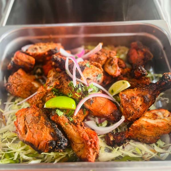 Tandoori chicken drumsticks and thighs, garnished with red onions, cilantro, and lime wedges, in a metal pan.