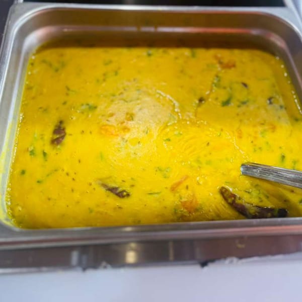 A close-up of a large metal tray filled with vibrant yellow Indian curry, garnished with green herbs.