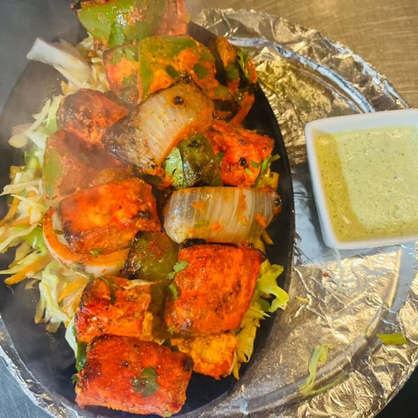 Sizzling paneer tikka with onions and bell peppers, served with a side of green chutney.