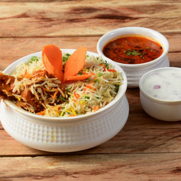 Chicken Biryani with gravy and raita, served in white bowls on a wooden table.