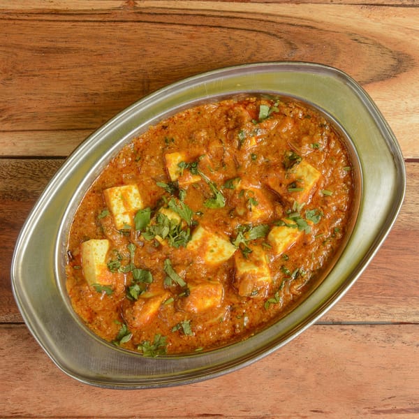 Paneer butter masala, an Indian dish with paneer cheese in a rich orange gravy, garnished with cilantro.