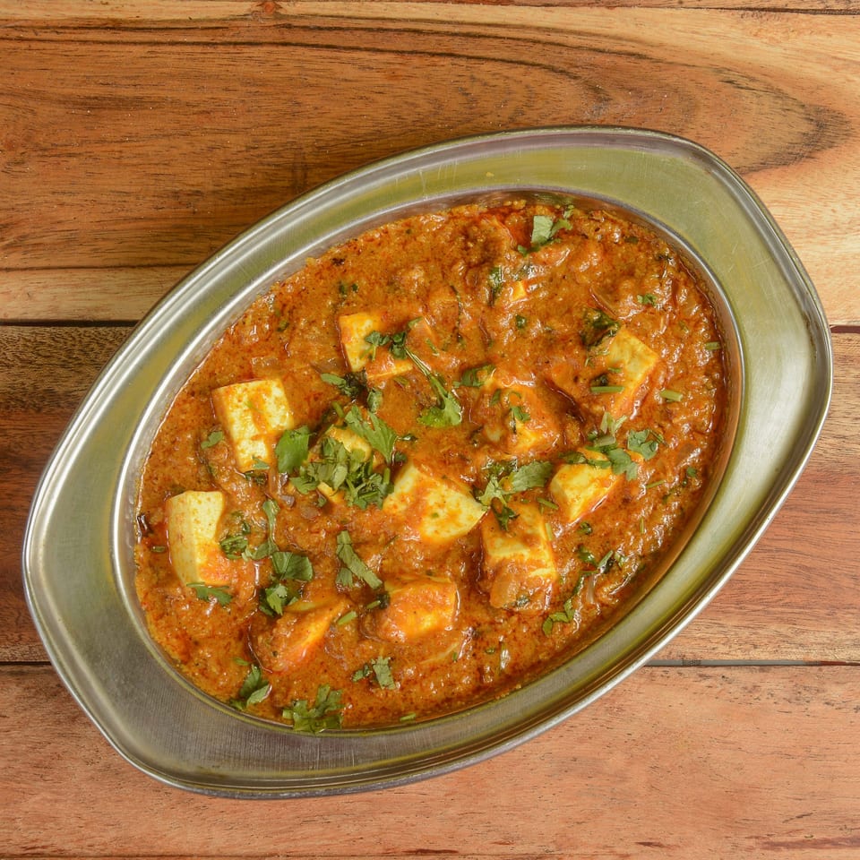 Paneer butter masala, an Indian dish with paneer cheese in a rich orange gravy, garnished with cilantro.