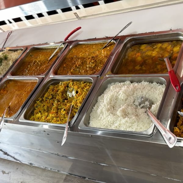 A buffet line with several metal trays filled with various Indian dishes like curries and rice.