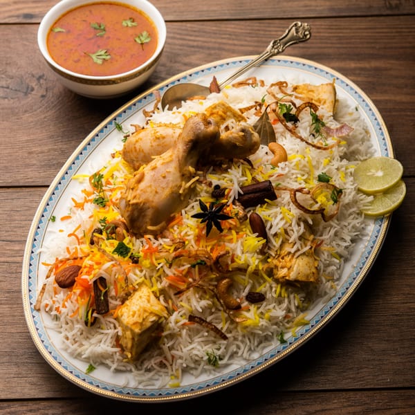 Chicken Biryani with rice, spices, and lemon slices, served with a side of curry.
