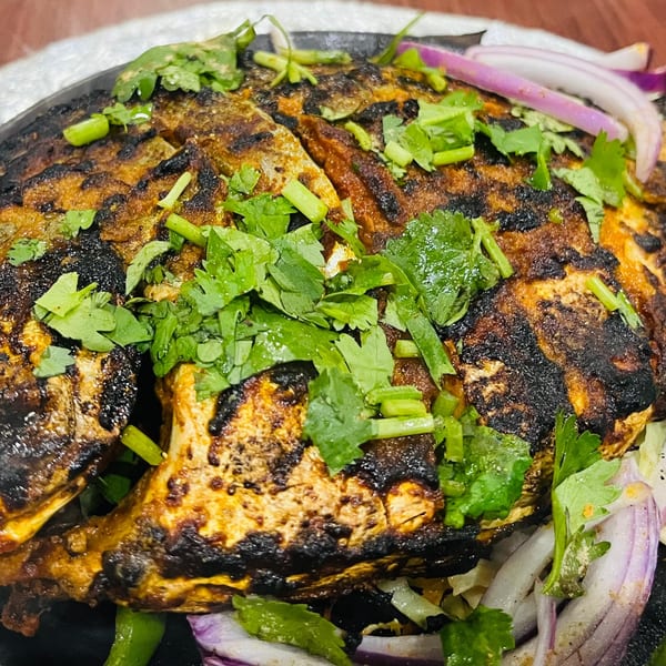 Close-up of a whole grilled fish, garnished with fresh cilantro and red onion slices.