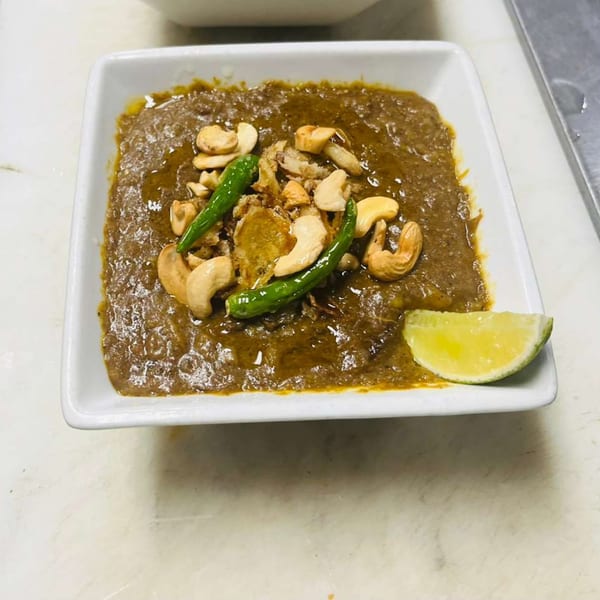 Haleem, a savory stew, garnished with cashews, green chilies, and a lime wedge in a white bowl.
