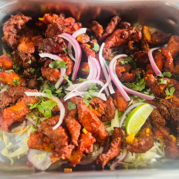 Close-up of crispy fried chicken pieces with red onion, cilantro, and a lime wedge.