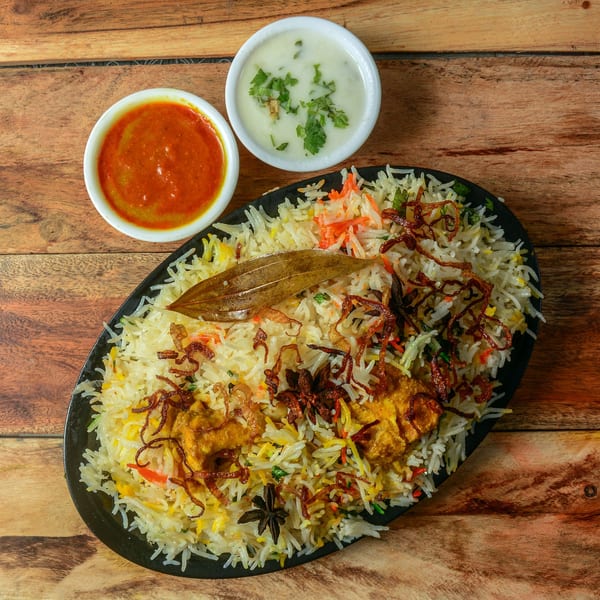 Chicken Biryani with fried onions, bay leaf, and star anise, served with two sauces.