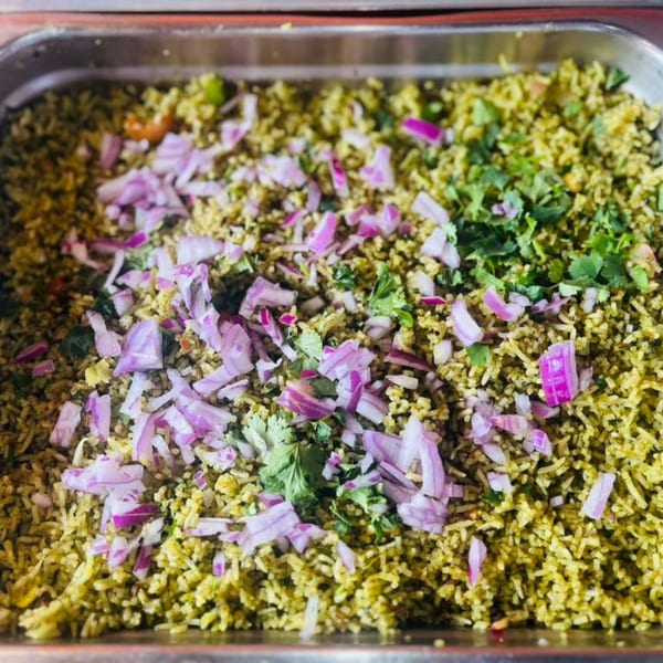Close-up of green rice pilaf topped with chopped red onions and fresh cilantro in a metal tray.